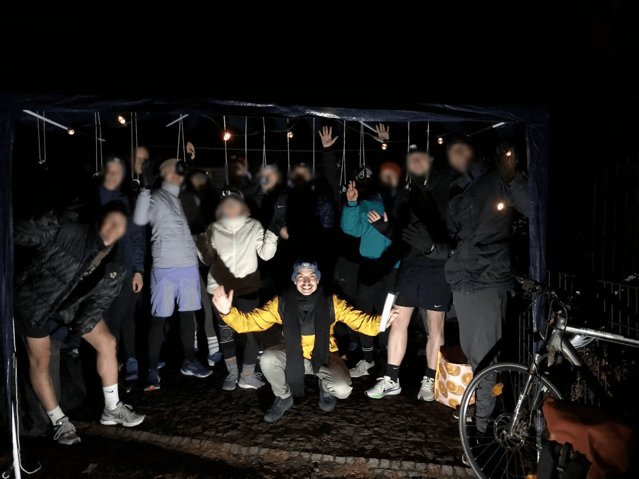 Große Gruppe von Läufer:innen mit Stirnlampen jubelt unter einer Lichterkette in einem Zelt